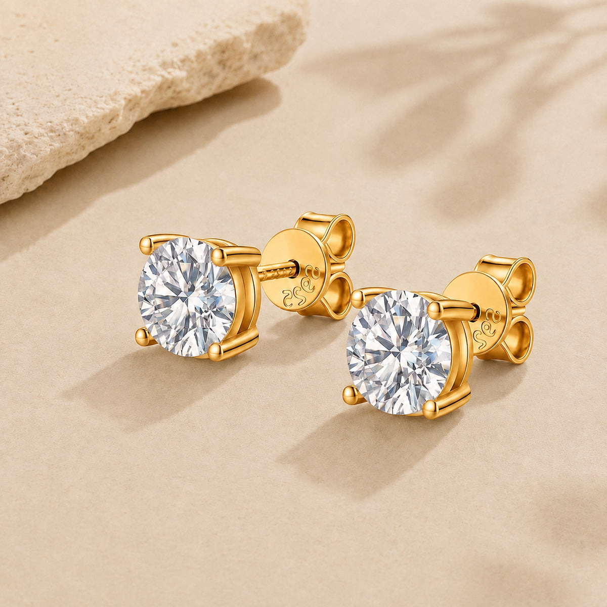 Gold moissanite stud earrings with round brilliant stones and 925 sterling silver setting on a beige background.