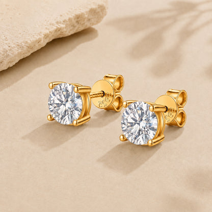 Gold moissanite stud earrings with round brilliant stones and 925 sterling silver setting on a beige background.