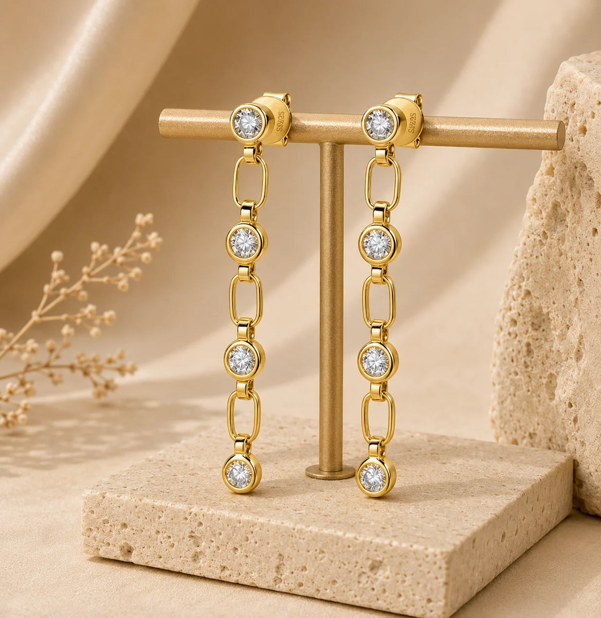 Liora gold linear drop earrings with linked sparkling round stones displayed on a beige stone stand.