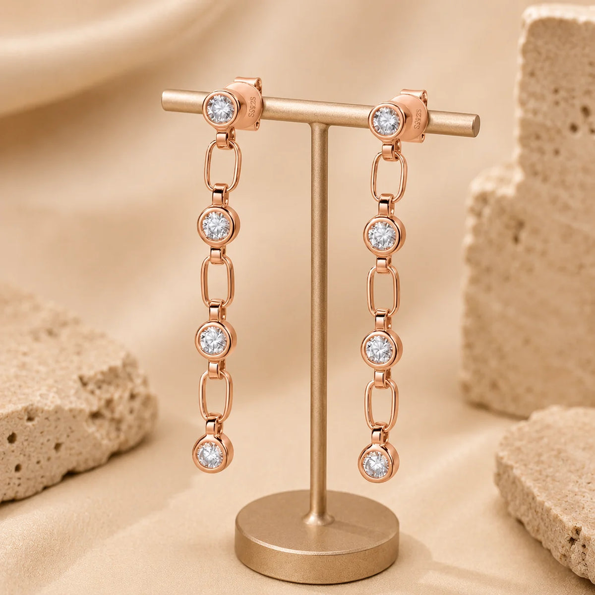 Liora rose gold linear drop earrings with sparkling round stones displayed on an elegant beige stand.