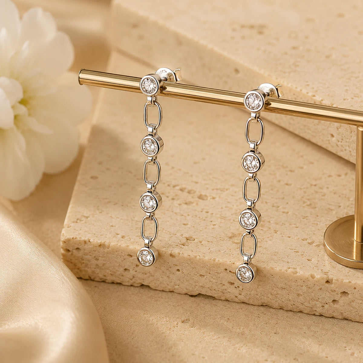 Detailed view of Liora silver linear drop earrings with linked round stones arranged on a beige jewelry surface.