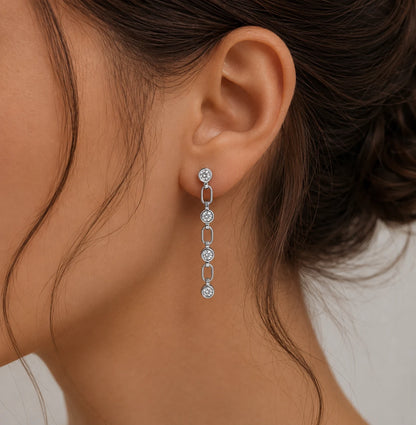 Detailed view of Liora silver linear drop earrings with linked round stones arranged on a beige jewelry surface.