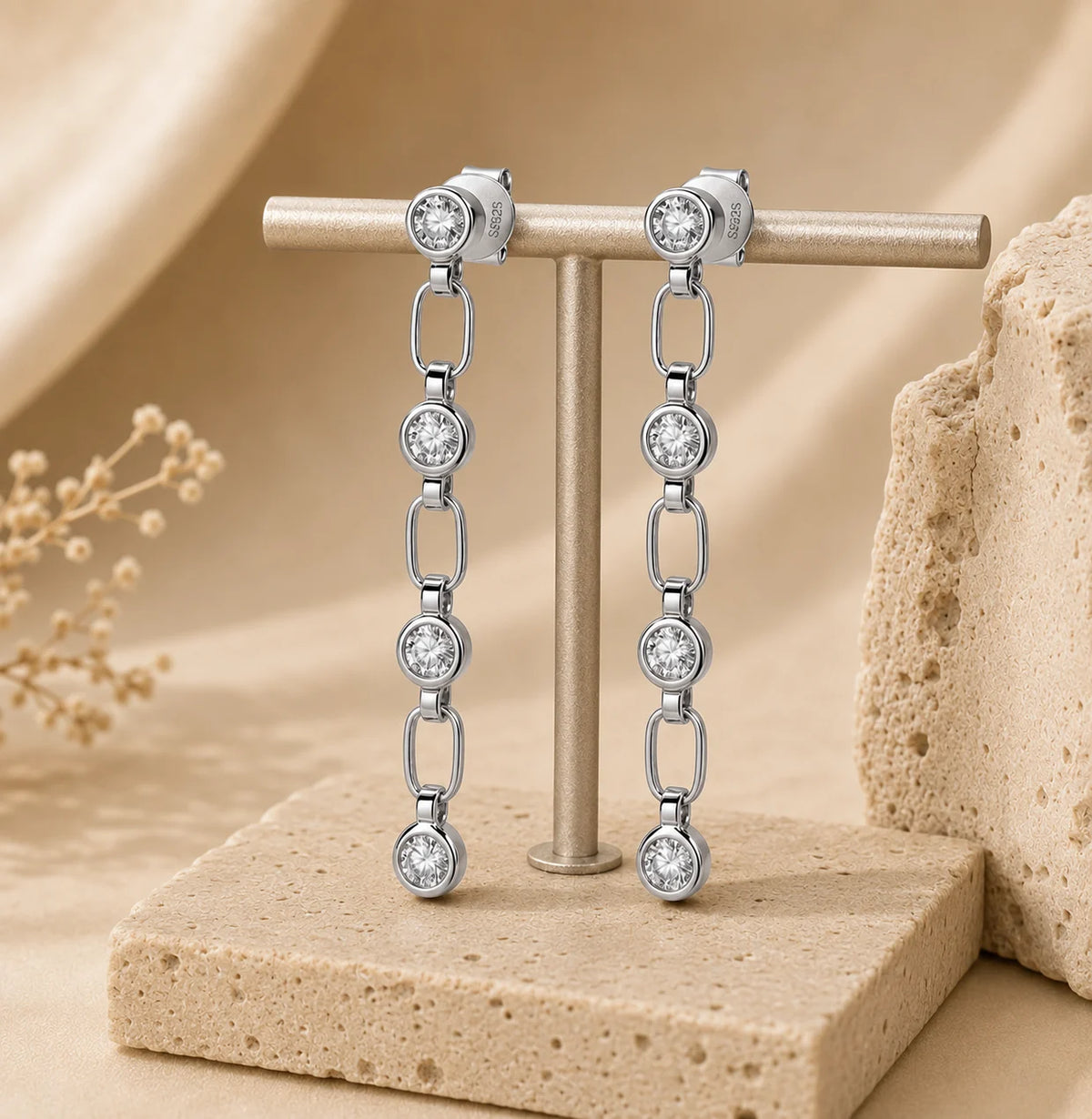 Front view of Liora 925 sterling silver linear drop earrings with linked brilliant-cut stones displayed on a beige jewelry stand.