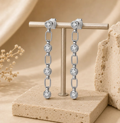 Front view of Liora 925 sterling silver linear drop earrings with linked brilliant-cut stones displayed on a beige jewelry stand.