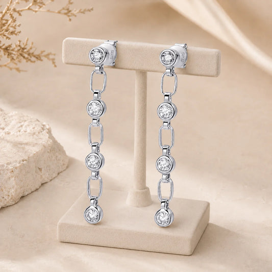 Front view of Liora sterling silver linear drop earrings displayed on a white stand against a beige background.
