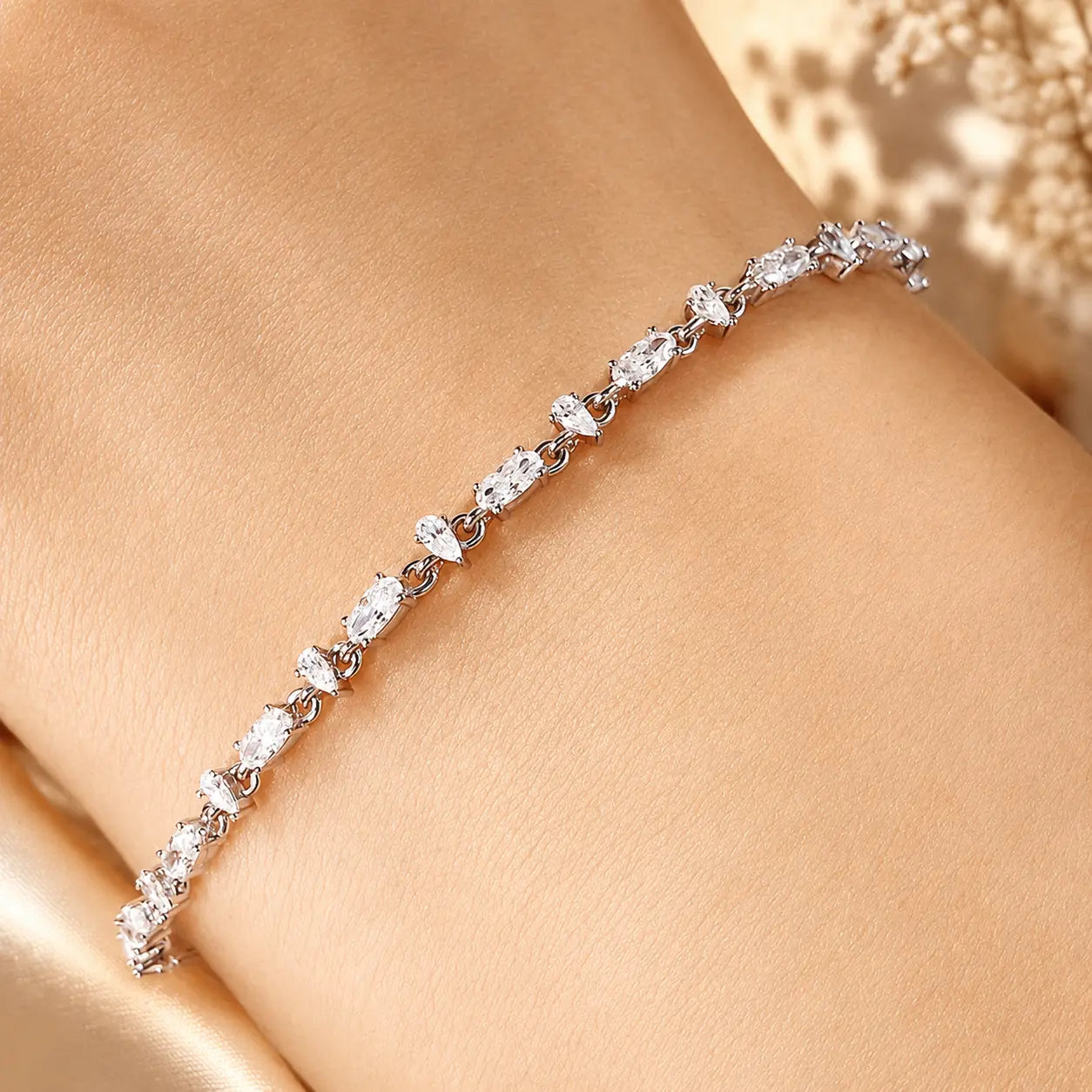 Woman wearing a sparkling mixed-cut moissanite tennis bracelet on her wrist in an elegant beige setting.