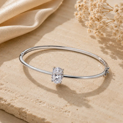 Silver 2CT oval-cut moissanite bangle bracelet for women displayed on a warm beige stone surface.