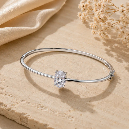 Silver 2CT oval-cut moissanite bangle bracelet for women displayed on a warm beige stone surface.