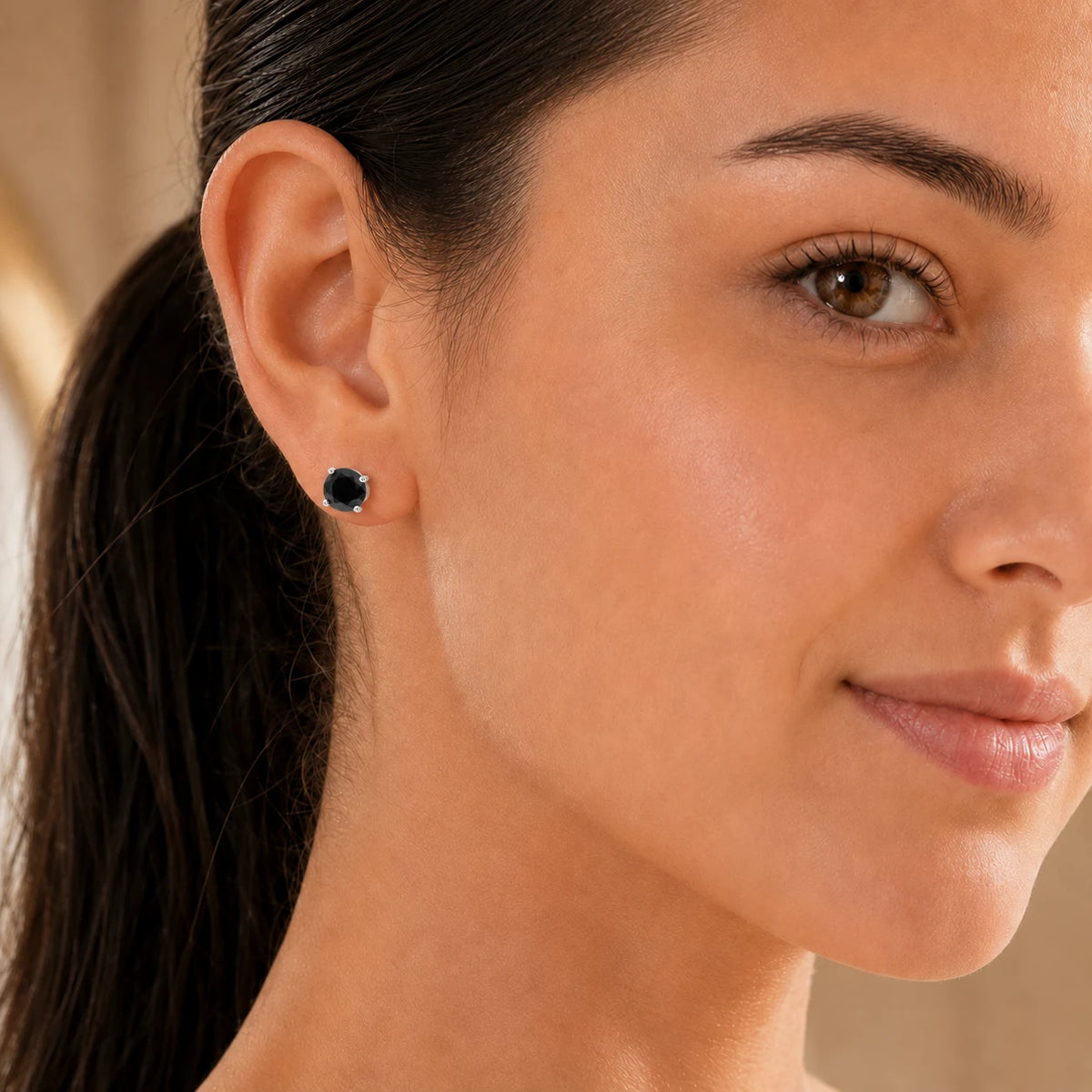 Woman wearing black round-cut gemstone stud earrings in a polished silver-tone four-prong setting.