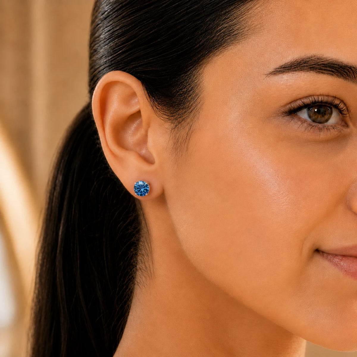 Close-up of a woman wearing vivid blue round-cut gemstone stud earrings with a classic silver-tone setting.