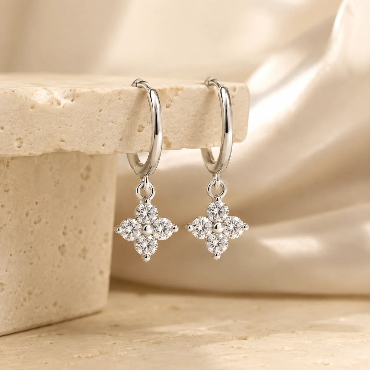Side view of Clovera™ Clover Moissanite Hoop Drop Earrings displayed on a warm beige stone surface.