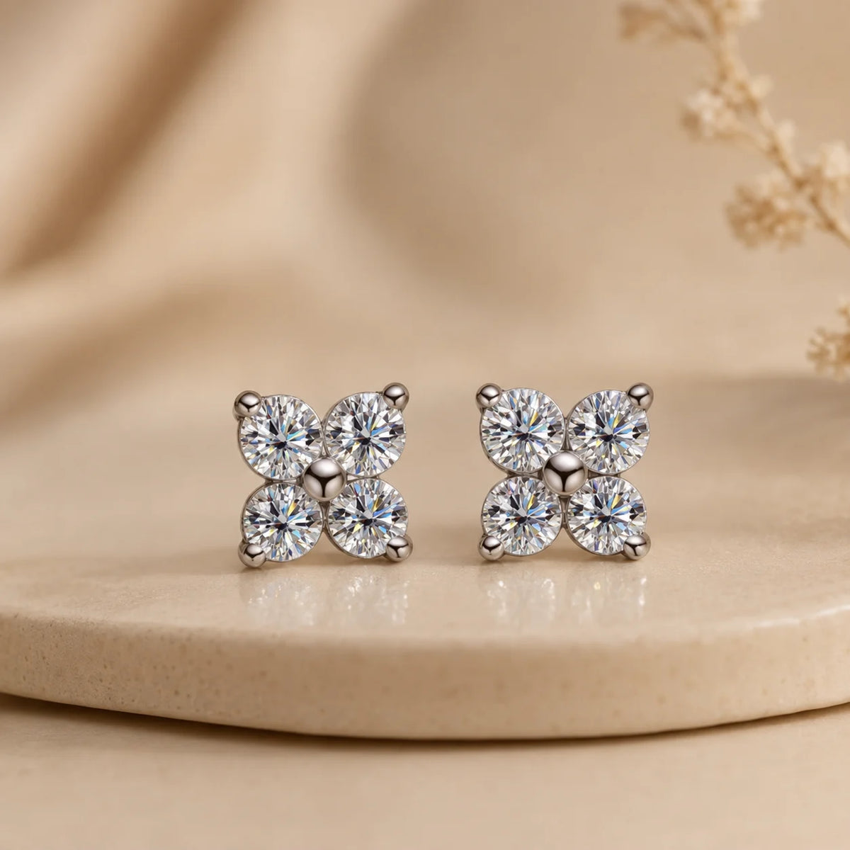 Elaris™ silver four-petal moissanite stud earrings displayed upright on a minimalist beige jewelry surface.