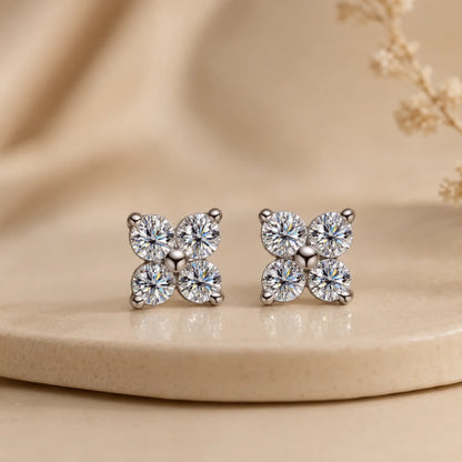 Elaris™ silver four-petal moissanite stud earrings displayed upright on a minimalist beige jewelry surface.