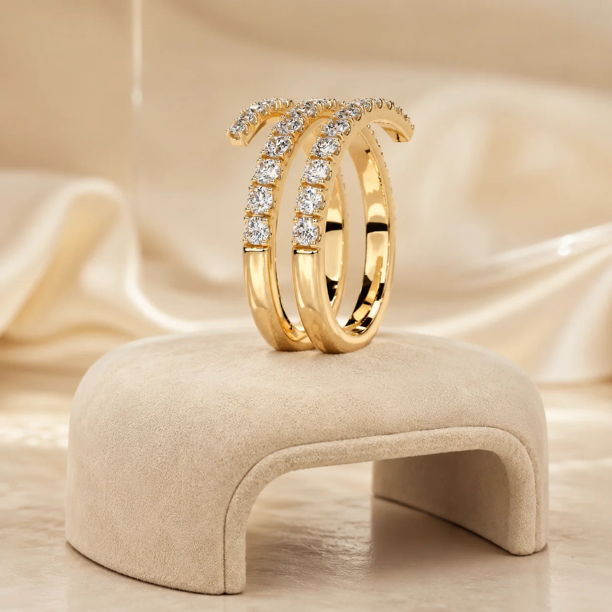 Gold three-row moissanite wrap ring displayed upright on a soft beige jewelry stand with a warm satin background.