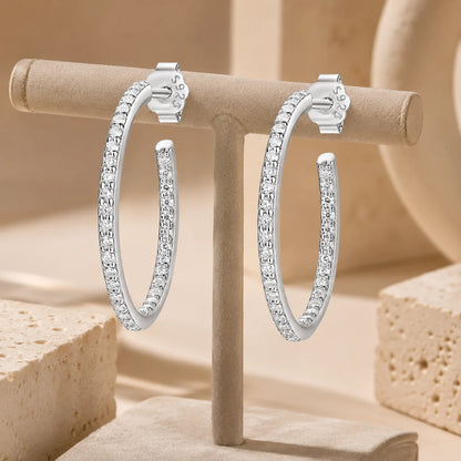 Isadora™ slim moissanite hoop earrings crafted in 925 sterling silver and displayed on a beige jewelry stand.