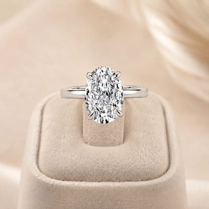 Silver Marlowe™ Oval Moissanite Engagement Ring with a brilliant oval solitaire stone displayed on a beige jewelry stand.