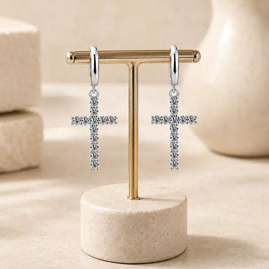 Silver-tone moissanite cross drop hoop earrings displayed on a minimalist beige jewelry stand.