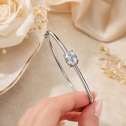Close-up of a silver oval-cut moissanite bangle bracelet held by hand, highlighting the solitaire stone and polished band.