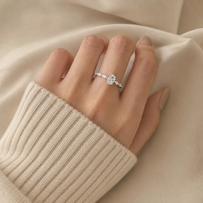 Woman wearing an oval-cut moissanite engagement ring with sparkling side stones on a polished silver band.