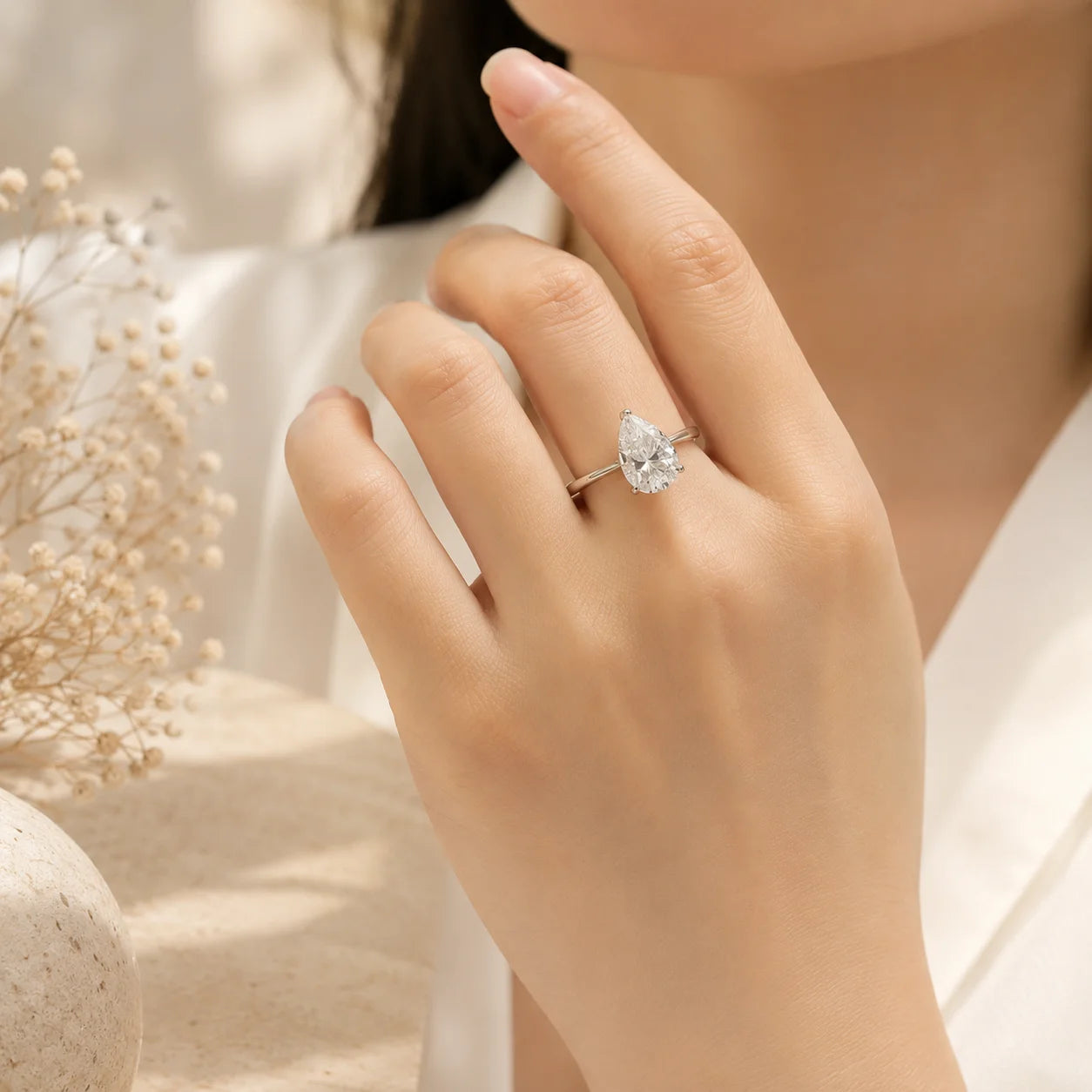 Close-up of a pear-cut moissanite engagement ring worn on a woman’s hand against a warm beige background.