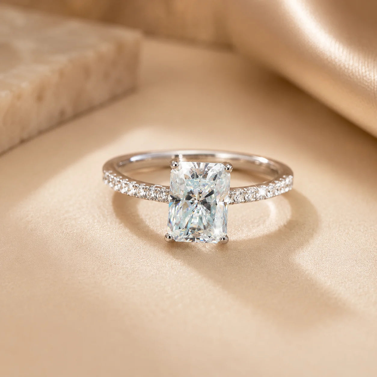 Front view of a radiant-cut moissanite engagement ring with a brilliant rectangular center stone and sparkling pavé band.
