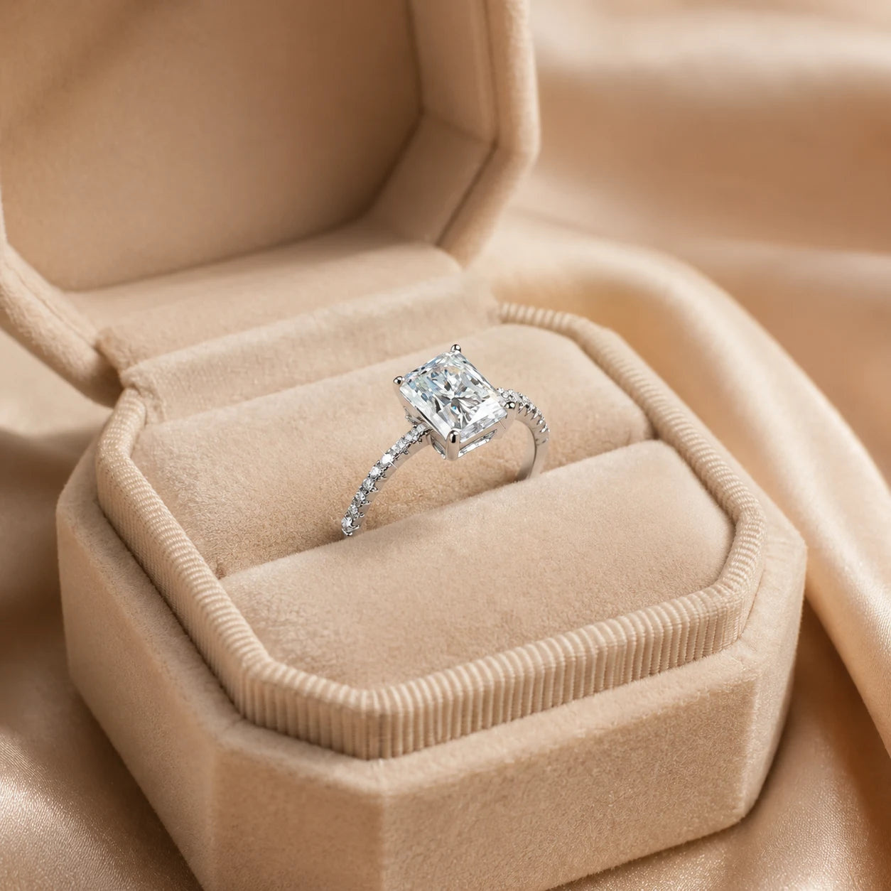 Radiant-cut moissanite engagement ring displayed inside an elegant beige velvet jewelry box with a pavé-set band.