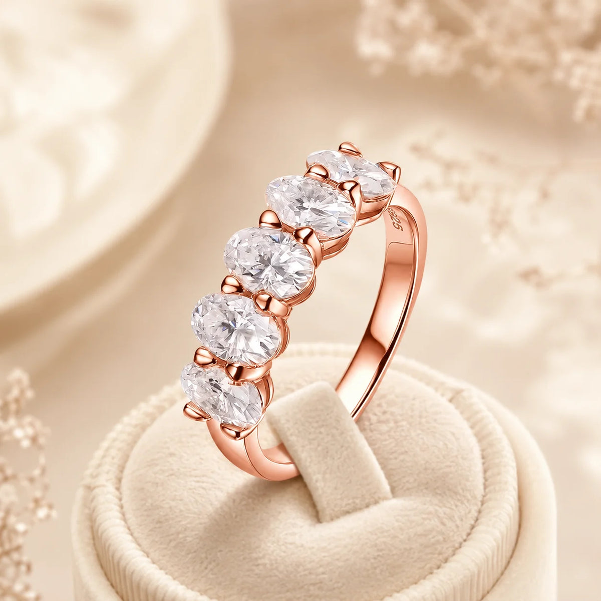 Rose gold five-stone moissanite anniversary ring with brilliant stones displayed on a beige velvet stand.