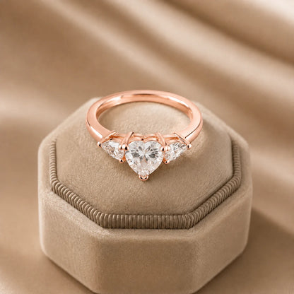 Rose gold heart-cut three-stone moissanite engagement ring featuring a brilliant center stone and two heart-shaped side stones.