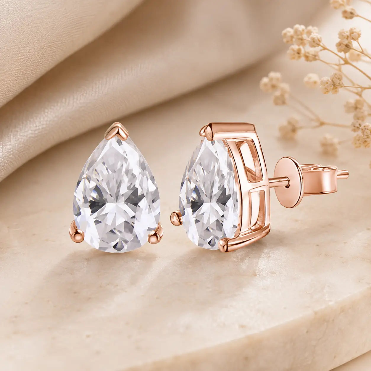 Rose gold pear-cut moissanite stud earrings with brilliant stones displayed on a warm beige luxury surface.