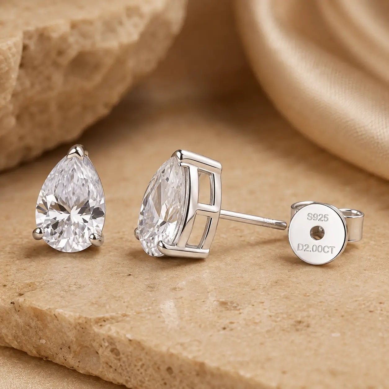 Close-up of pear-cut moissanite stud earrings showing the silver-tone setting, straight posts and S925 marked butterfly backs.