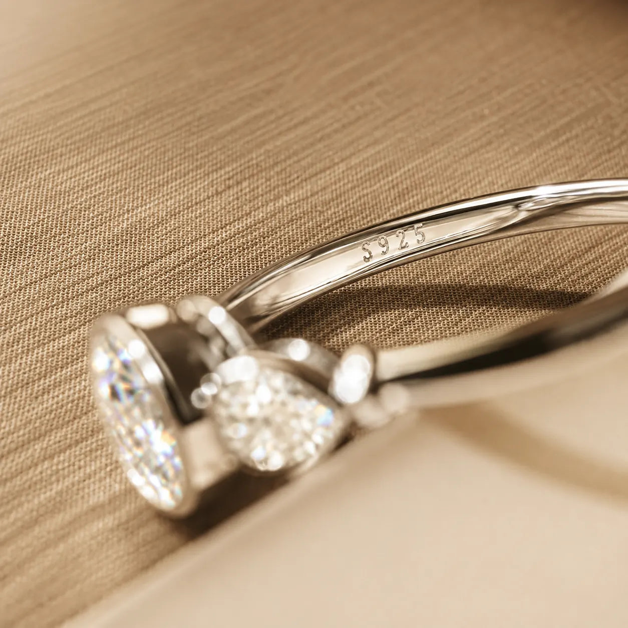 Side view of a three-stone moissanite ring showing the raised settings, polished silver band and S925 hallmark.
