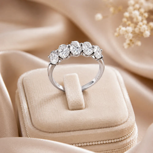 Silver five-stone moissanite anniversary ring displayed on an elegant beige jewelry box with a satin background.