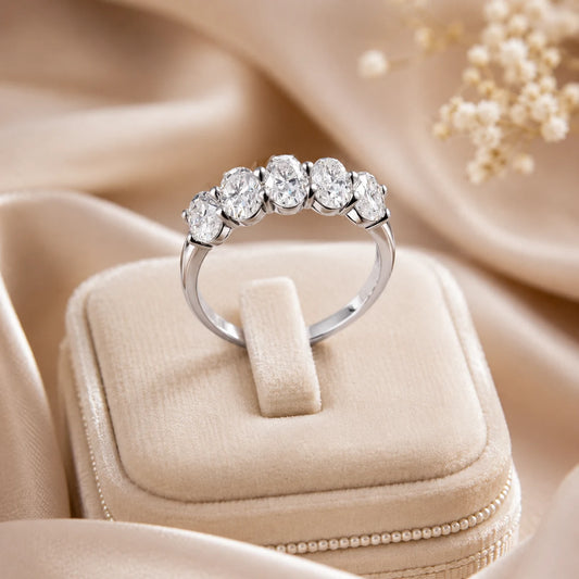 Silver five-stone moissanite anniversary ring displayed on an elegant beige jewelry box with a satin background.