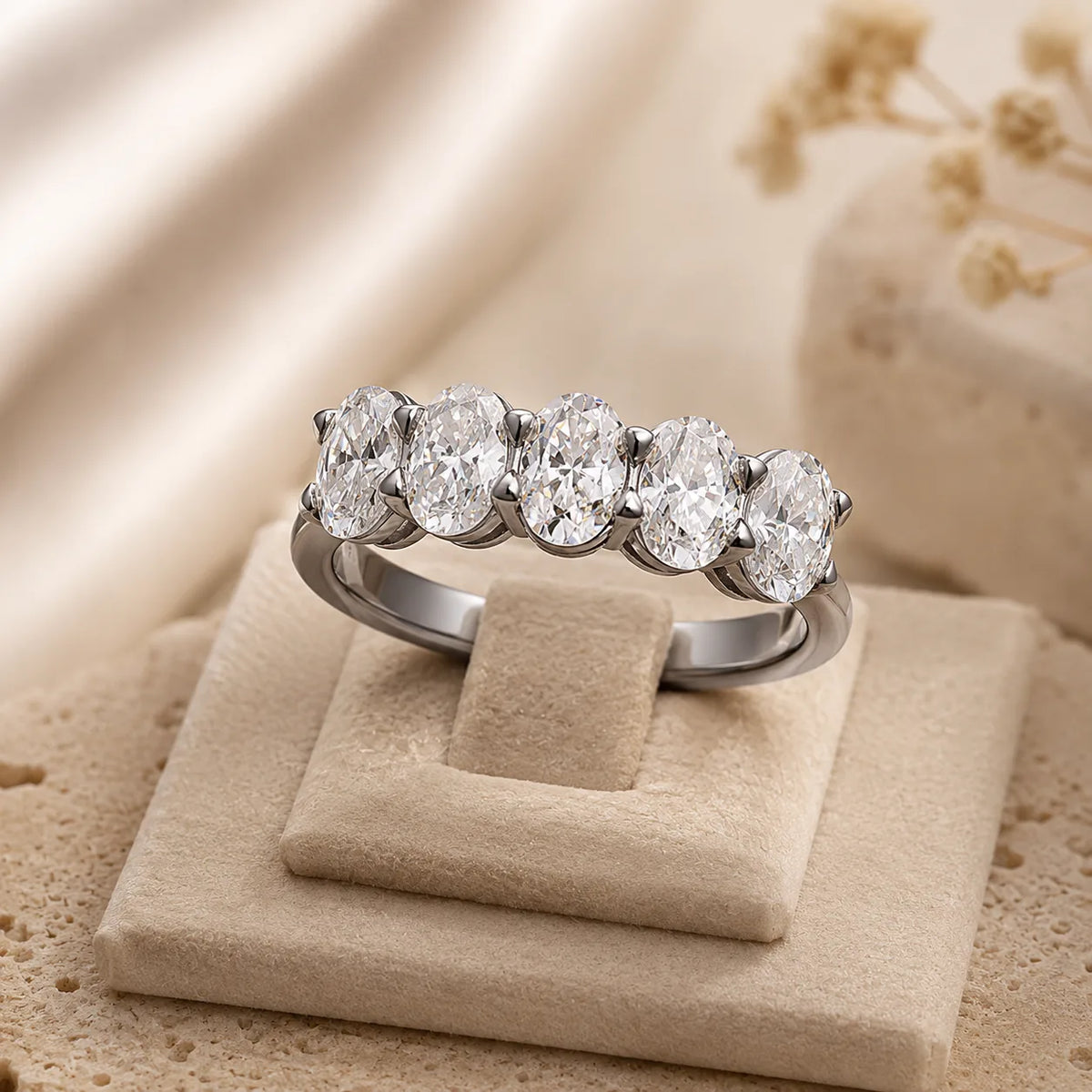 Front view of a silver five-stone moissanite ring displayed on a soft beige jewelry stand.