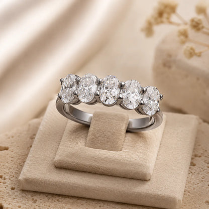 Front view of a silver five-stone moissanite ring displayed on a soft beige jewelry stand.