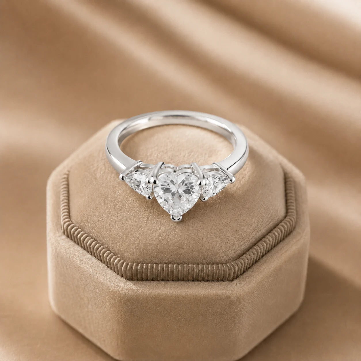 Silver heart-cut three-stone moissanite engagement ring displayed on an elegant beige velvet jewelry box.