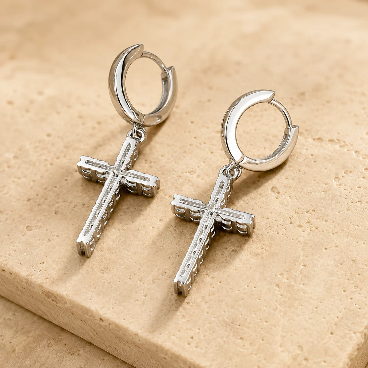 Close-up of silver-tone hoop earrings with dangling cross charms set with sparkling moissanite stones.