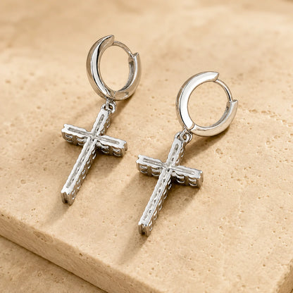 Close-up of silver-tone hoop earrings with dangling cross charms set with sparkling moissanite stones.