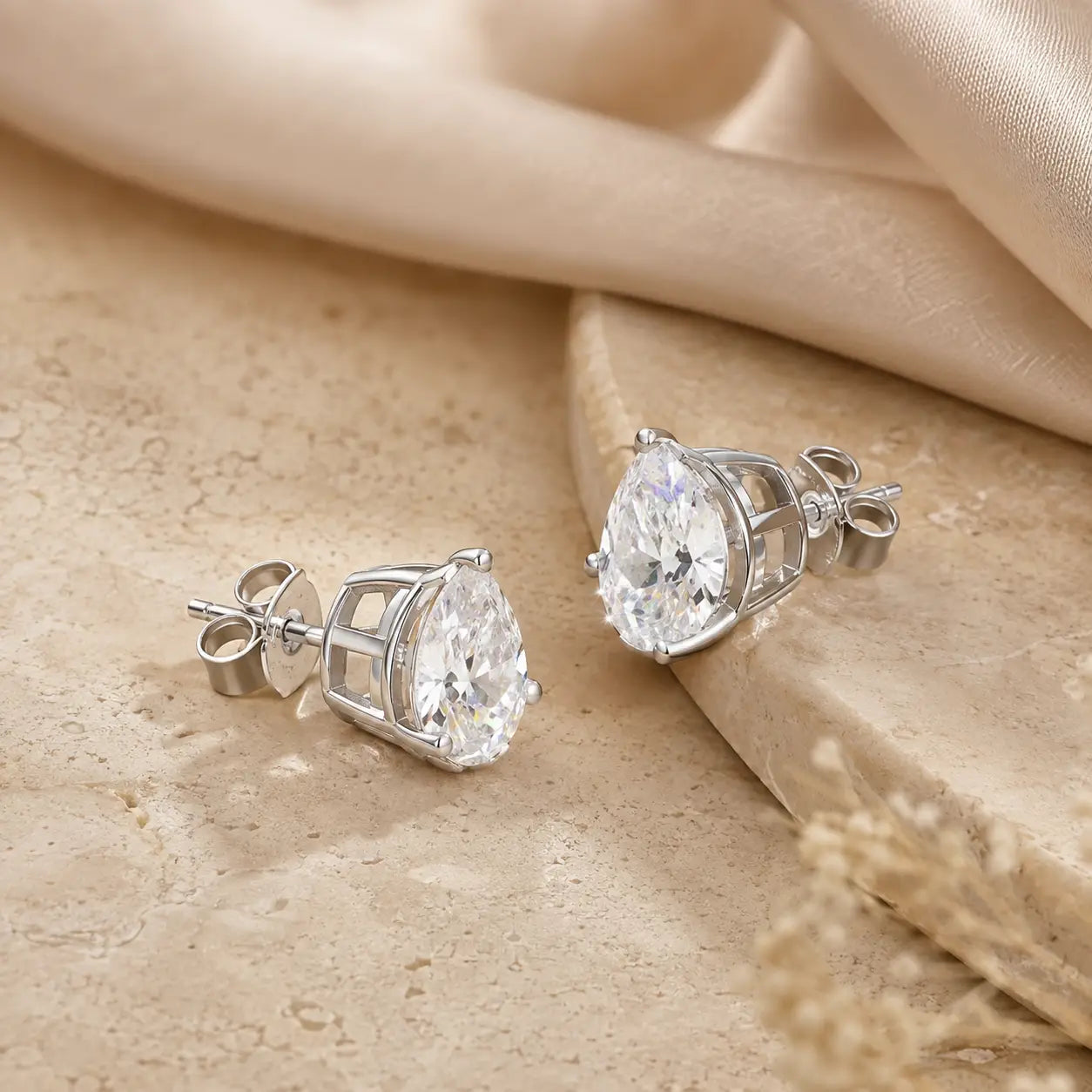Front and back views of silver pear-cut moissanite stud earrings showing the prong settings and secure posts.