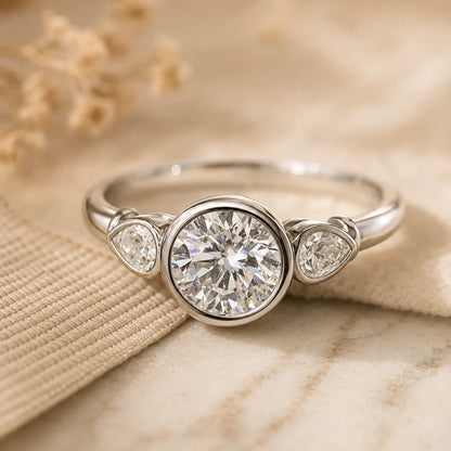 Silver three-stone ring featuring a bezel-set round moissanite center stone and two sparkling side stones.
