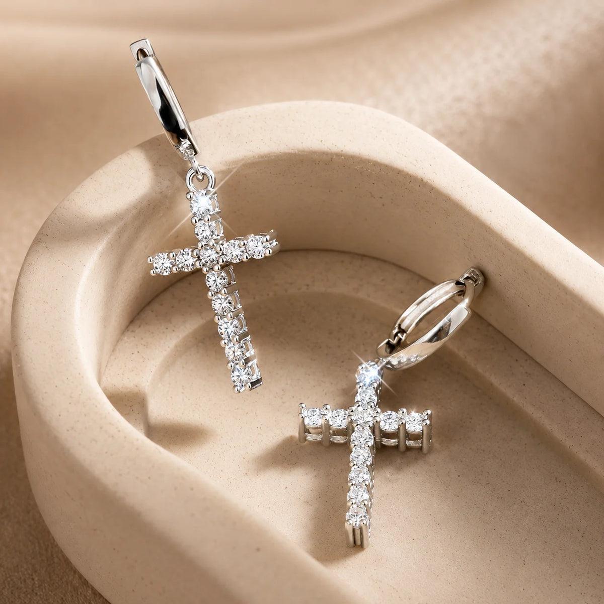 Silver-tone moissanite cross hoop earrings arranged inside an elegant beige jewelry tray.