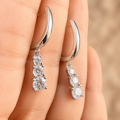 Detailed close-up of sterling silver huggie drop earrings with three graduated round brilliant-cut stones.