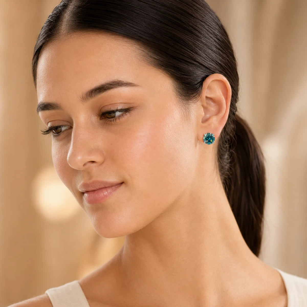 Woman wearing teal blue-green round-cut gemstone stud earrings for an elegant everyday look.
