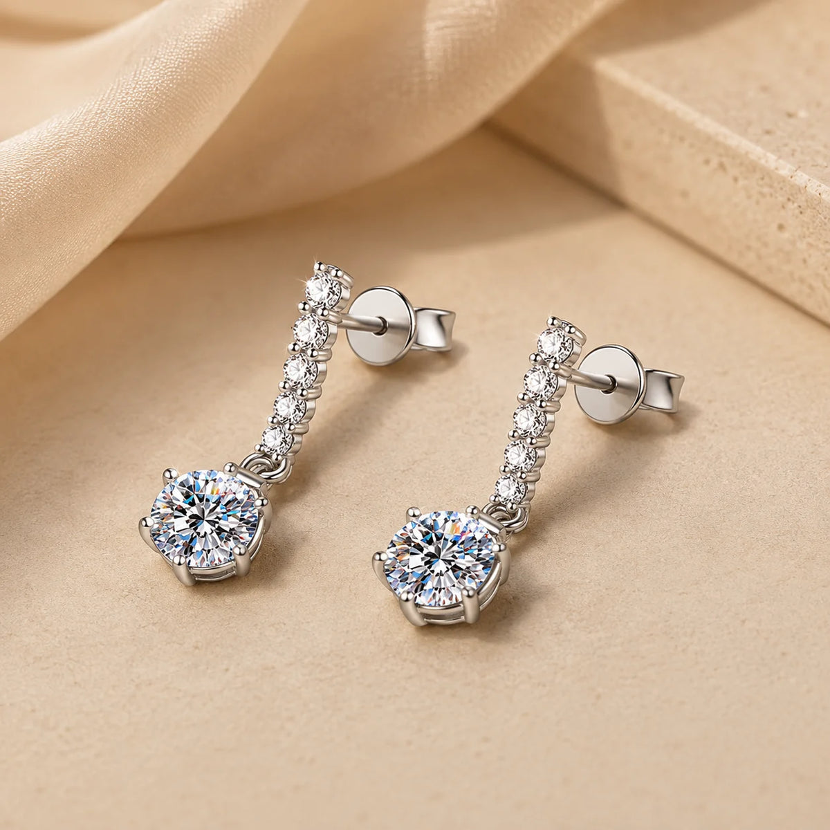 Valenne™ 2CT Moissanite Drop Stud Earrings resting on a soft beige surface with delicate drop detailing.
