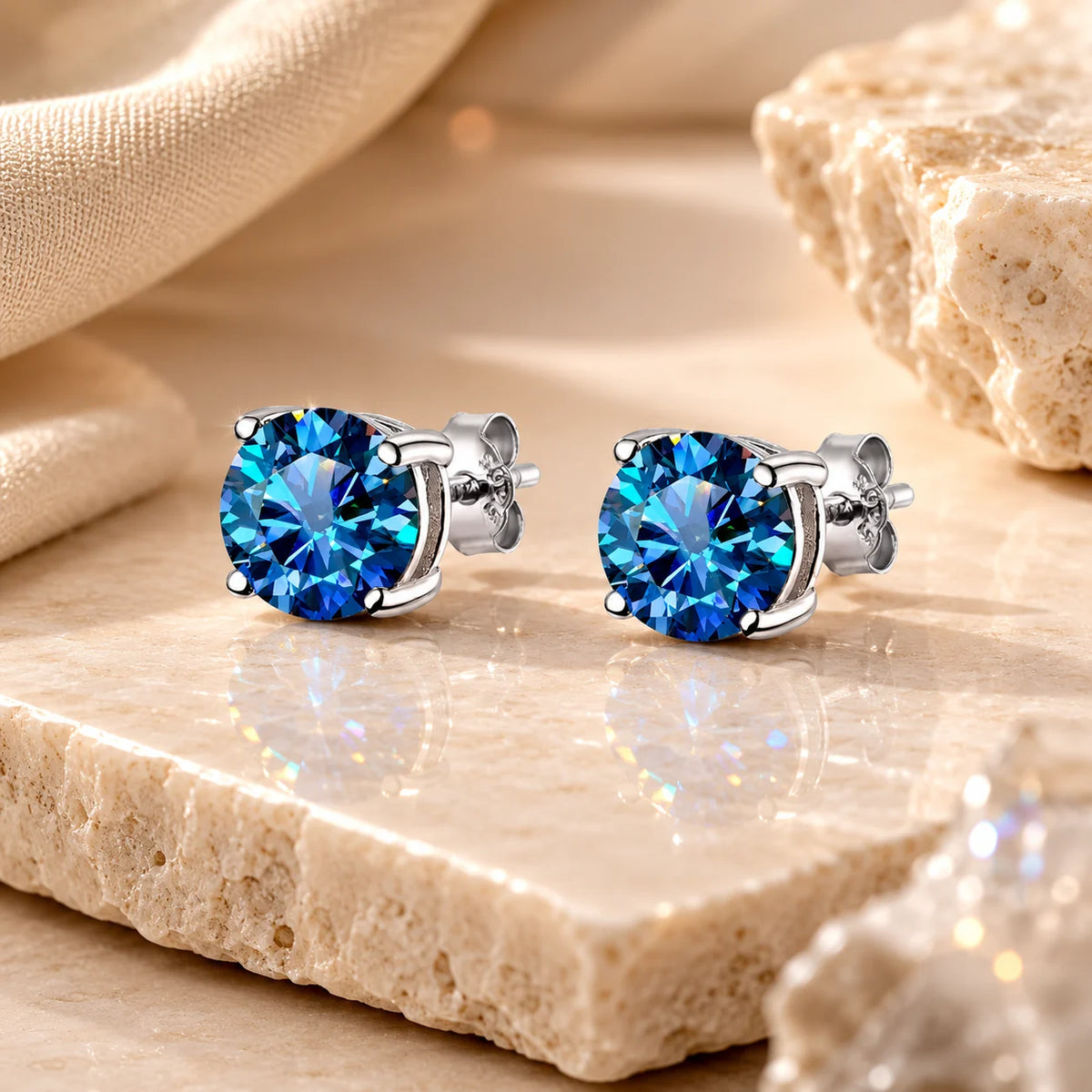 Eloryva vivid blue round-cut gemstone stud earrings with brilliant sparkle on a warm beige stone display.