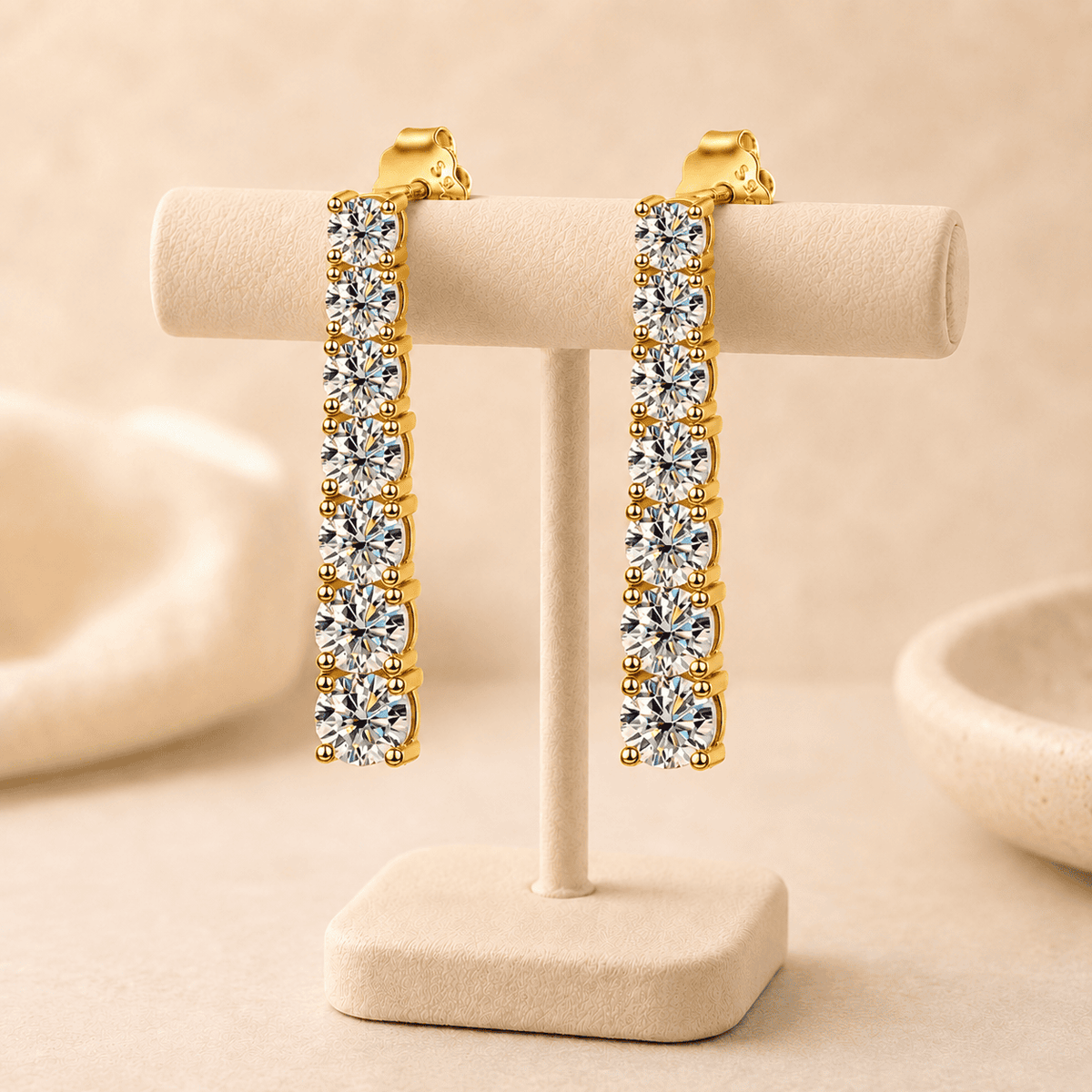 Gold moissanite drop earrings displayed on a beige jewelry stand with sparkling stones and refined luxury styling.