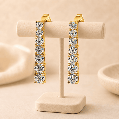 Gold moissanite drop earrings displayed on a beige jewelry stand with sparkling stones and refined luxury styling.