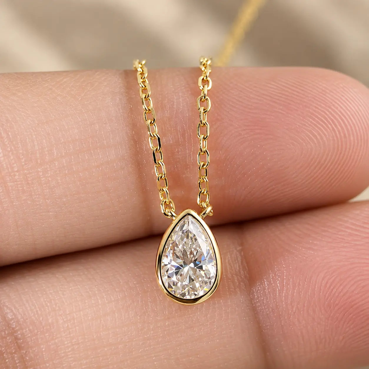 Close-up detail of a pear cut moissanite pendant on a fine gold tone chain