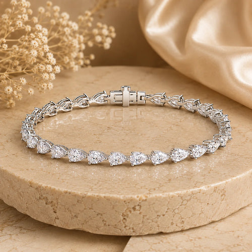 Front view of the Langley™ pear-cut moissanite tennis bracelet for women with sparkling stones and a secure clasp on a beige stone surface.