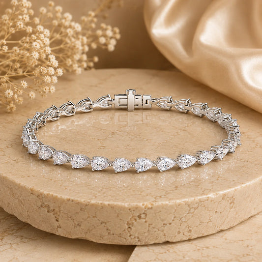 Front view of the Langley™ pear-cut moissanite tennis bracelet for women with sparkling stones and a secure clasp on a beige stone surface.